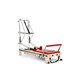 Elina Pilates Twin Reformer aus Ahornholz mit roten Polstern, Schrägansicht mit Turm auf weißem Hintergrund