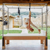 Elina Pilates Wooden Cadillac aus Rock-Ahorn, Frau übt kopfüber im Trapez auf einer Terrasse