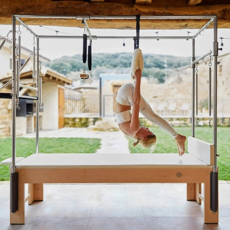 Elina Pilates Wooden Cadillac aus Rock-Ahorn, Frau übt kopfüber im Trapez auf einer Terrasse