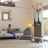 Elina Pilates Vertikaler Reformer senkrecht im Wohnzimmer, eine Frau sitzt auf dem Sofa