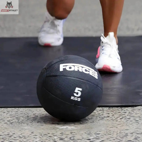Force USA Medizinball 9 kg, Ball in der 5-kg-Ausführung liegt auf der Matte vor den Füßen einer Trainierenden