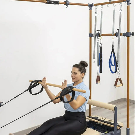 Hegren Pilates Wooden Stick 1,10 m aus Eiche, Frau zieht den Stab am Cadillac-Reformer mit Seilen zur Brust