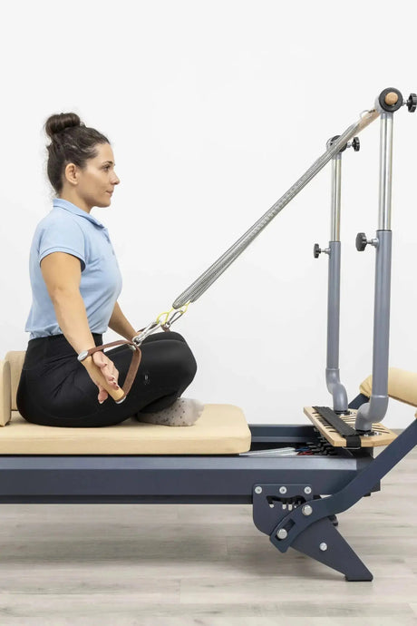 Hegren Stability Bar für den TALMA 62, Frau sitzt im Schneidersitz auf dem Reformer und greift die Stange