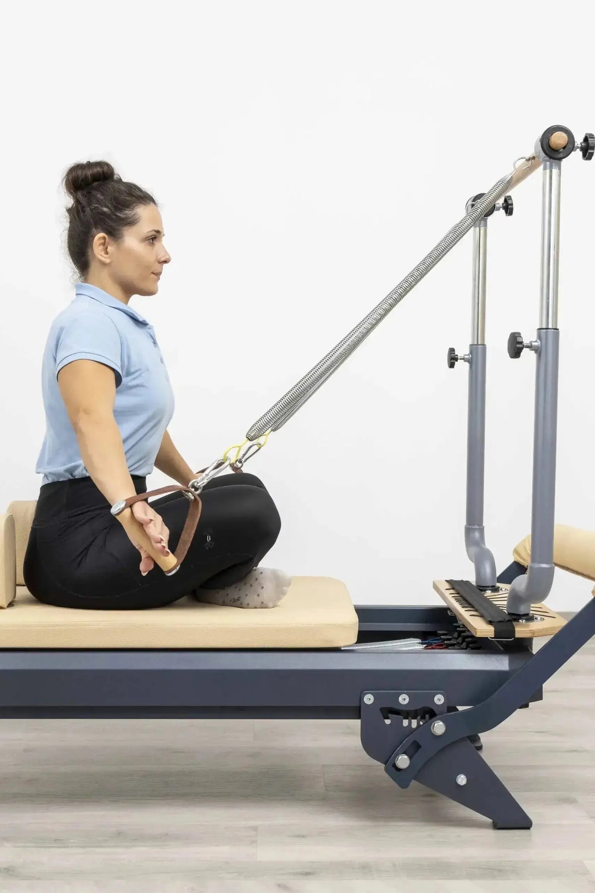 Hegren Stability Bar Wall Stand Wandhalter: Stability Bar am Reformer, Trainierende sitzt im Schneidersitz und zieht den Griff