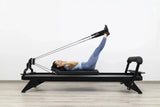 Hegren TALMA 62 Black Elegance Reformer mit Frau in Rückenlage beim Beinzug, Seitenansicht