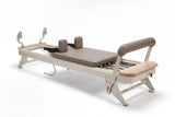 Hegren TALMA 62 Reformer mit Box und Jumpboard in Schrägansicht mit hellem Rahmen und taupefarbenen Polstern freigestellt