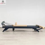 Hegren TALMA 62 Reformer mit Box und Jumpboard in Seitenansicht mit dunklem Rahmen und beigen Polstern auf hellem Holzboden