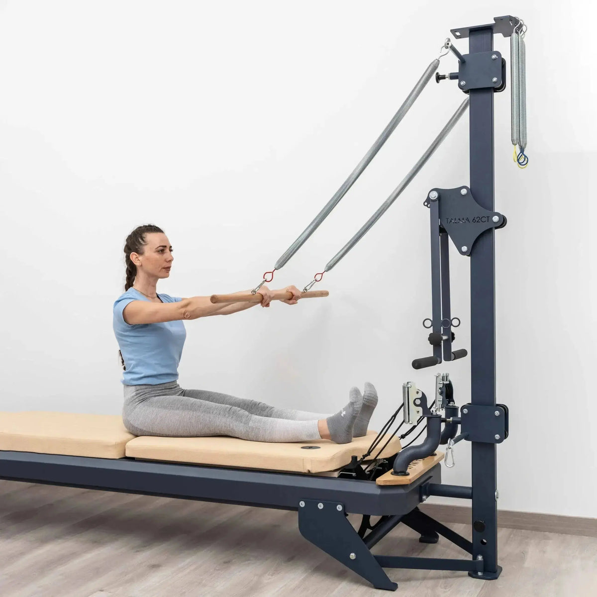 Hegren TALMA 62CT+ Reformer mit Tower, Frau trainiert im Sitzen mit der Stange am Tower