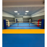 SportCom Bodenanker-Boxring mit Stahlpfosten in einer Halle, Frontansicht mit blauer und roter Ecke