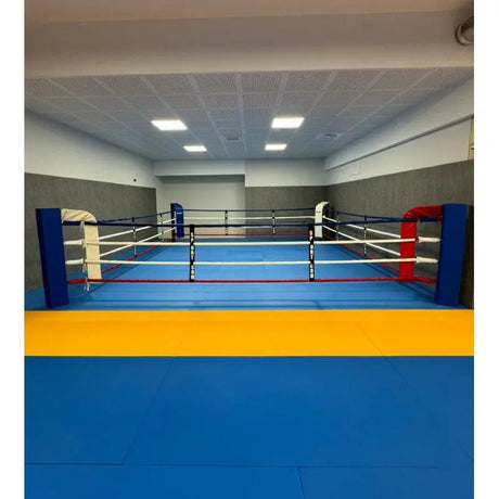 SportCom Bodenanker-Boxring mit Stahlpfosten in einer Halle, Frontansicht mit blauer und roter Ecke