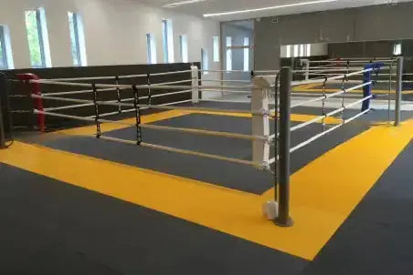 SportCom Bodenanker-Boxring mit Stahlpfosten auf gelber und grauer Matte, Schrägansicht