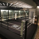SportCom Boxring-Individualisierung: schwarzer Ring mit weißen Ecken und Logo in einem Studio mit Glasfront