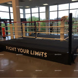 SportCom Boxring-Schürze aus Cordura mit Aufdruck Fight Your Limits an einem Ring vor großer Fensterfront
