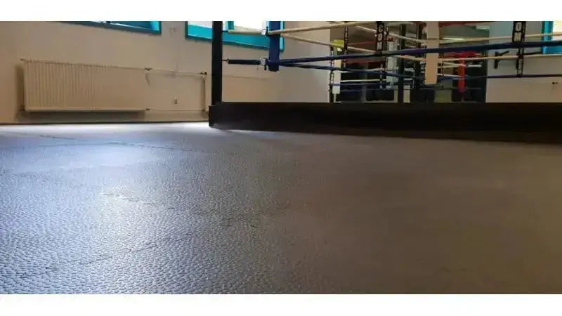 SportCom Cross-Training Puzzlematte verlegt als durchgehender grauer Boden in einer Trainingshalle mit Boxring
