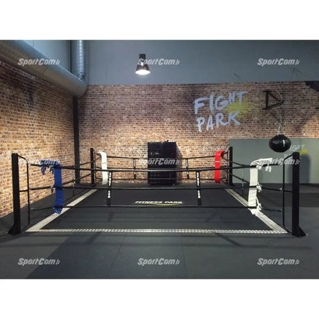 SportCom Ecofix Bodenmontage-Boxring mit Aluminiumrand, vor Backsteinwand mit blauer und weißer Ecke, frontal