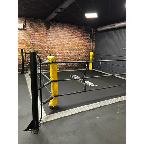 SportCom Ecofix Bodenmontage-Boxring mit Aluminiumrand, mit gelben Eckpolstern vor einer Backsteinwand