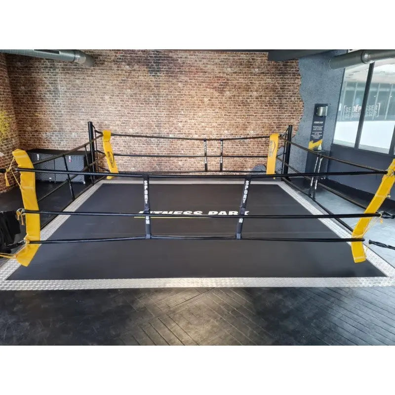 SportCom Ecofix Bodenmontage-Boxring mit Aluminiumrand, vor einer Backsteinwand mit gelben Eckpolstern