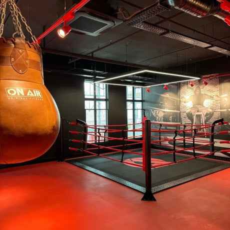 SportCom Ecofix Bodenmontage-Boxring mit Aluminiumrand, mit Sandsack im Vordergrund und rotem Boden