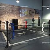 SportCom Ecofix Bodenmontage-Boxring mit Aluminiumrand, in einem Gym mit Wandschriftzug und blauer Ecke