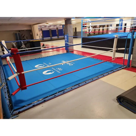 SportCom Ecofix Bodenmontage-Boxring mit Spannseilen, mit blauem Boden und Logo, Schrägansicht in der Halle