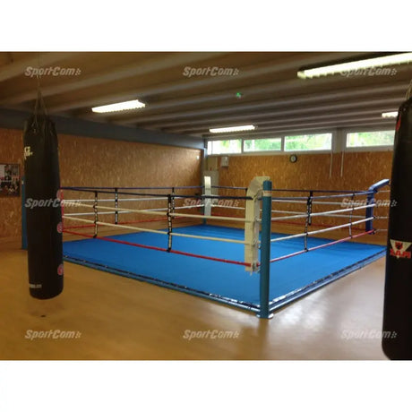 SportCom Ecofix Boxring mit Bodenhülsen und Spannseilen, mit blauem Boden in einer Halle mit Sandsack