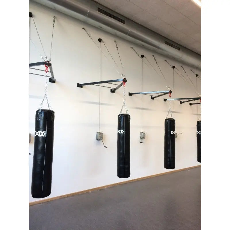 SportCom Faltbare Sandsackhalterung mit Handwinde: mehrere Boxsäcke an Halterungen entlang einer langen Hallenwand
