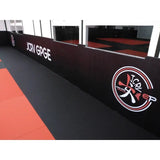 SportCom Flexi-Wall Wandschutz von Dollamur in Schwarz mit Vereinslogo an der Wand über roter Matte