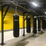 SportCom Förderschiene mit Rahmen für Sandsäcke, in einem Gym mit gelber Wand und schwarzen Sandsäcken