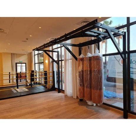 SportCom Förderschiene mit Rahmen für Sandsäcke, in einem Gym mit Glasfront und hellen Sandsäcken