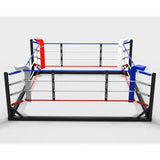 SportCom Freistehender Boxring 4x4 m, Frontansicht mit roter und blauer Ecke, weißen Neutralecken und schwarzem Boden