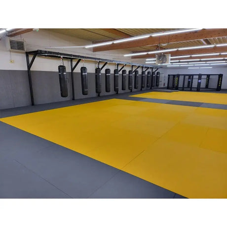 SportCom Judo-Tatami Reisstroh 1 × 1 m, 5 cm, rutschfeste Unterseite, gelbe Fläche mit grauem Rand, Sandsäcke an der Wand