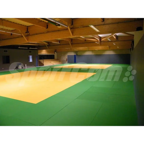SportCom Judo-Tatami Reisstroh 1 × 1 m, 5 cm, rutschfeste Unterseite, grüne Fläche mit gelbem Feld in einer Halle mit Holzdecke