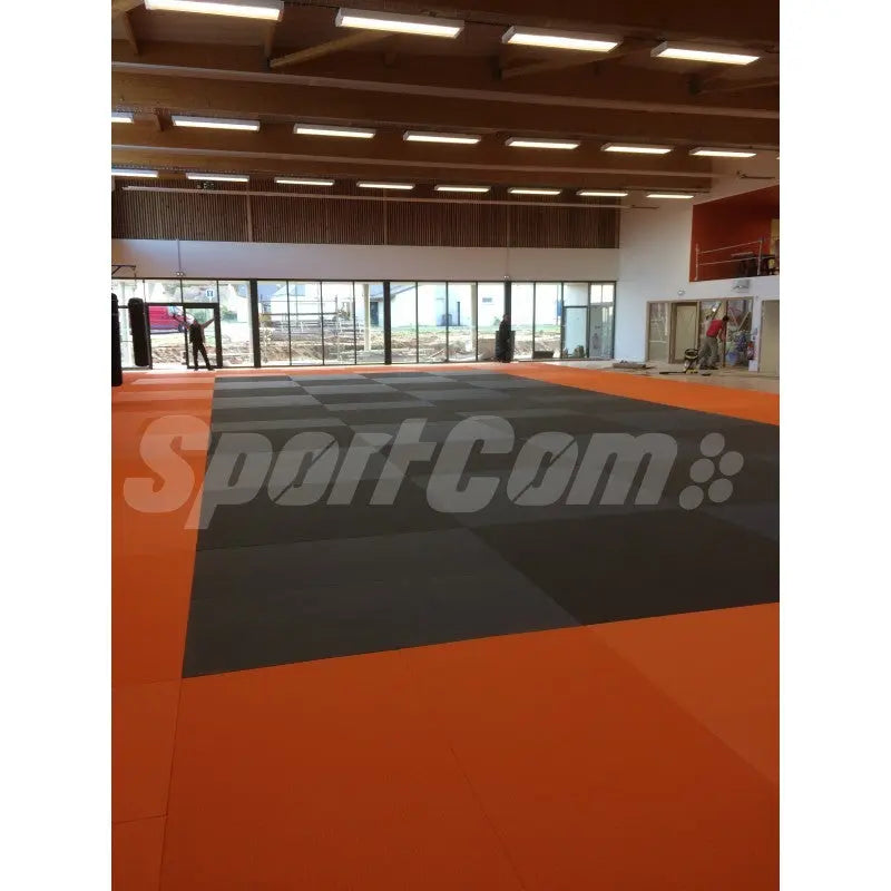 SportCom Judo-Tatami Reisstroh 1 × 1 m, 5 cm, rutschfeste Unterseite, orange Fläche mit dunklem Feld in heller Halle