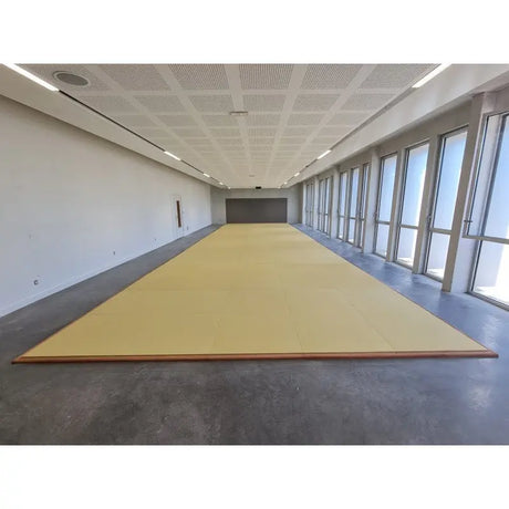 SportCom Judo-Tatami Reisstroh 1 × 1 m, 5 cm, rutschfeste Unterseite, gelbe Fläche in einem langen hellen Raum