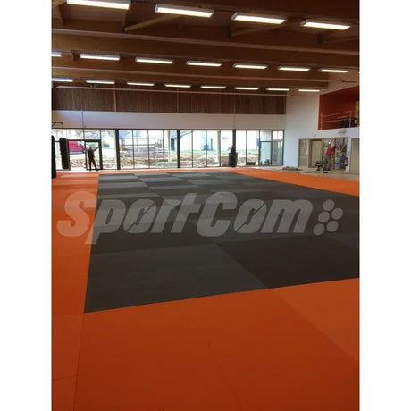 SportCom Judo-Tatami Reisstroh 2 × 1 m, 5 cm, glatte Unterseite, orange Fläche mit grauer Zone in Halle mit Fensterfront