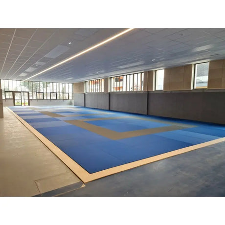 SportCom Judo-Tatami Reisstroh 2 × 1 m, 5 cm, glatte Unterseite, blau-graue Fläche mit Holzrahmen in moderner Halle
