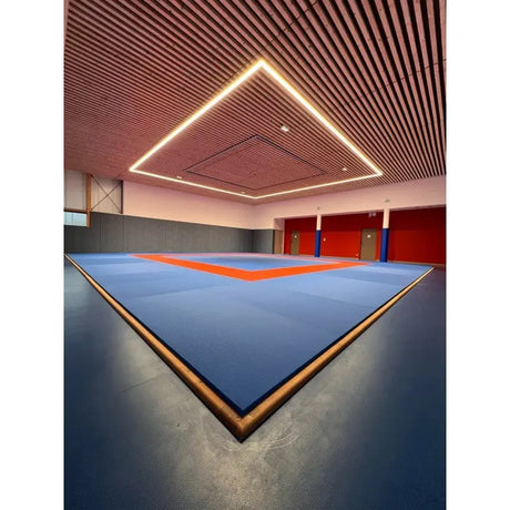 SportCom Judo-Tatami Reisstroh 2 × 1 m, 5 cm, glatte Unterseite, blaue Fläche mit rotem Rahmen unter einer Holzlamellendecke