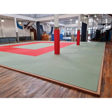 SportCom Judo-Tatami Reisstroh 2 × 1 m, 5 cm, glatte Unterseite, grüne Fläche mit roter Zone in Halle mit roten Säulen