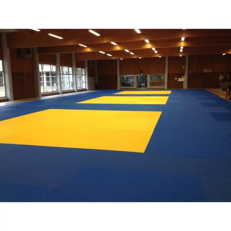 SportCom Judo-Tatami Reisstroh 2 × 1 m, 5 cm, glatte Unterseite, große gelbe Zonen auf Blau in einer Holzhalle