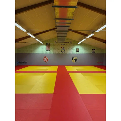 SportCom Judo-Tatami Reisstroh 2 × 1 m, 5 cm, glatte Unterseite, rote Fläche mit gelben Zonen in einer Holzhalle