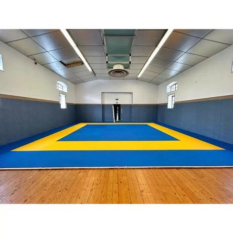 SportCom Judo-Tatami Reisstroh 2 × 1 m, 5 cm, glatte Unterseite, blaues Quadrat mit gelber Umrandung auf Parkett, Frontansicht