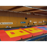 SportCom Judo-Tatami Reisstroh 2 × 1 m, 5 cm, glatte Unterseite, rote Fläche mit gelben Kampfzonen in großer Sporthalle