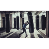 SportCom Kunstleder-Sandsack 1,80 m im Einsatz beim Boxtraining in einer Halle mit mehreren Säcken