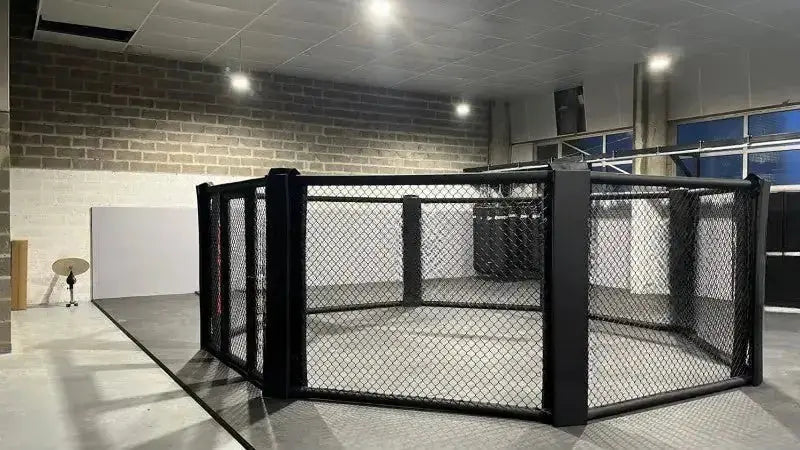 SportCom MMA-Käfig Oktagon zur Bodenmontage, in einer Halle mit blauen Fenstern, seitlich