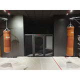 SportCom MMA-Paneel mit Tür als Käfigfront zwischen zwei braunen Boxsäcken
