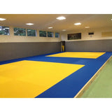SportCom MMA-Tatami Glattfinish 1 × 1 m, 5 cm, glatte Unterseite, helle Halle mit gelben Feldern auf blauem Grund