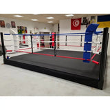 SportCom Pro-Trainingsboxring mit 30 cm Podium, in der Boxhalle mit Flaggen aus seitlicher Perspektive