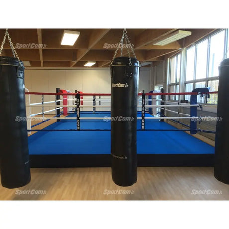 SportCom Pro-Trainingsboxring mit 30 cm Podium, mit blauem Boden, Boxsäcke im Vordergrund