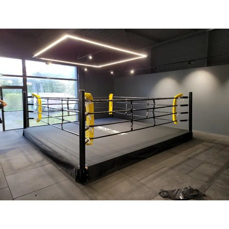 SportCom Pro-Trainingsboxring mit 30 cm Podium, mit gelben Eckpolstern vor einer Fensterfront