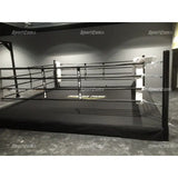 SportCom Pro-Trainingsboxring mit 30 cm Podium, in einer dunklen Halle mit schwarzen Seilen